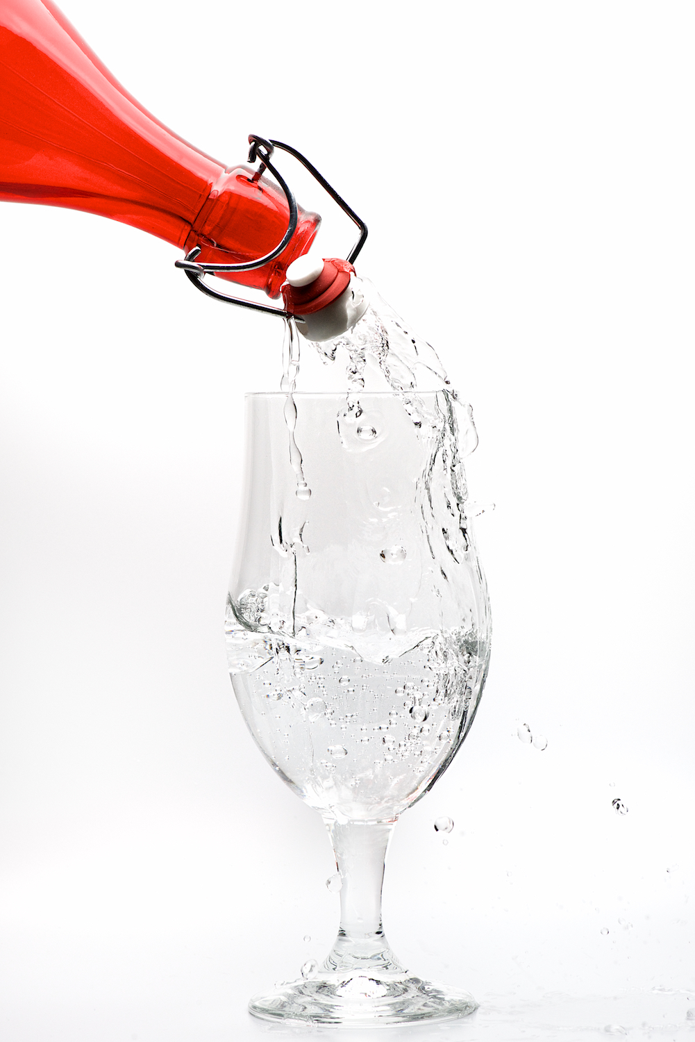 Water pour splash from red bottle into stem glass on white background by Bret Doss Commercial Food & Product Photography  Seattle