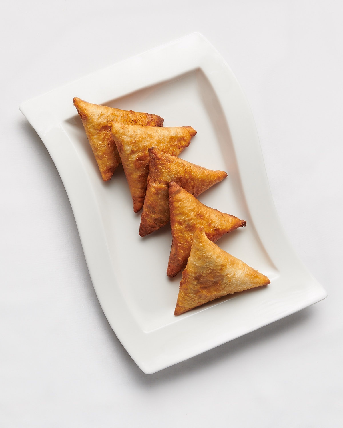 Sambusas Samosas on white wave-style plate on white tablecloth by Bret Doss Commercial Food & Product Photography  Seattle