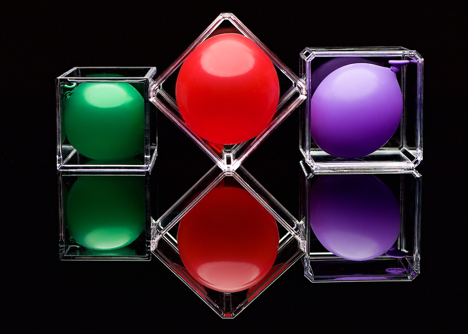 green red purple balloons in acrylic boxes on black reflective surface abstract by Bret Doss Commercial Product Photography Seattle
