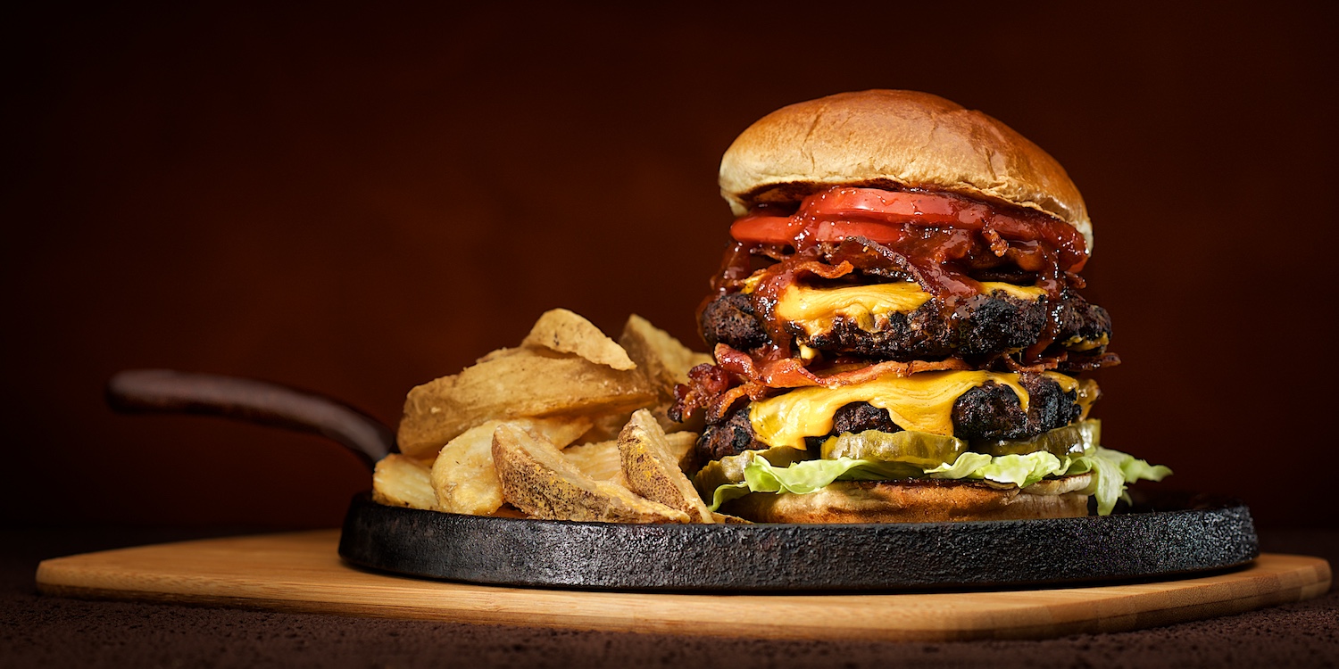 double bacon cheeseburger with house fries served on cast iron in warm light on dark background  by Bret Doss Commercial Food & Product Photography  Seattle
